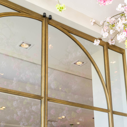 Messing stalen schuifdeur met glas en sierlijke boogdetails, elegant gecombineerd met bloesemdecoratie in een luxe interieur.
